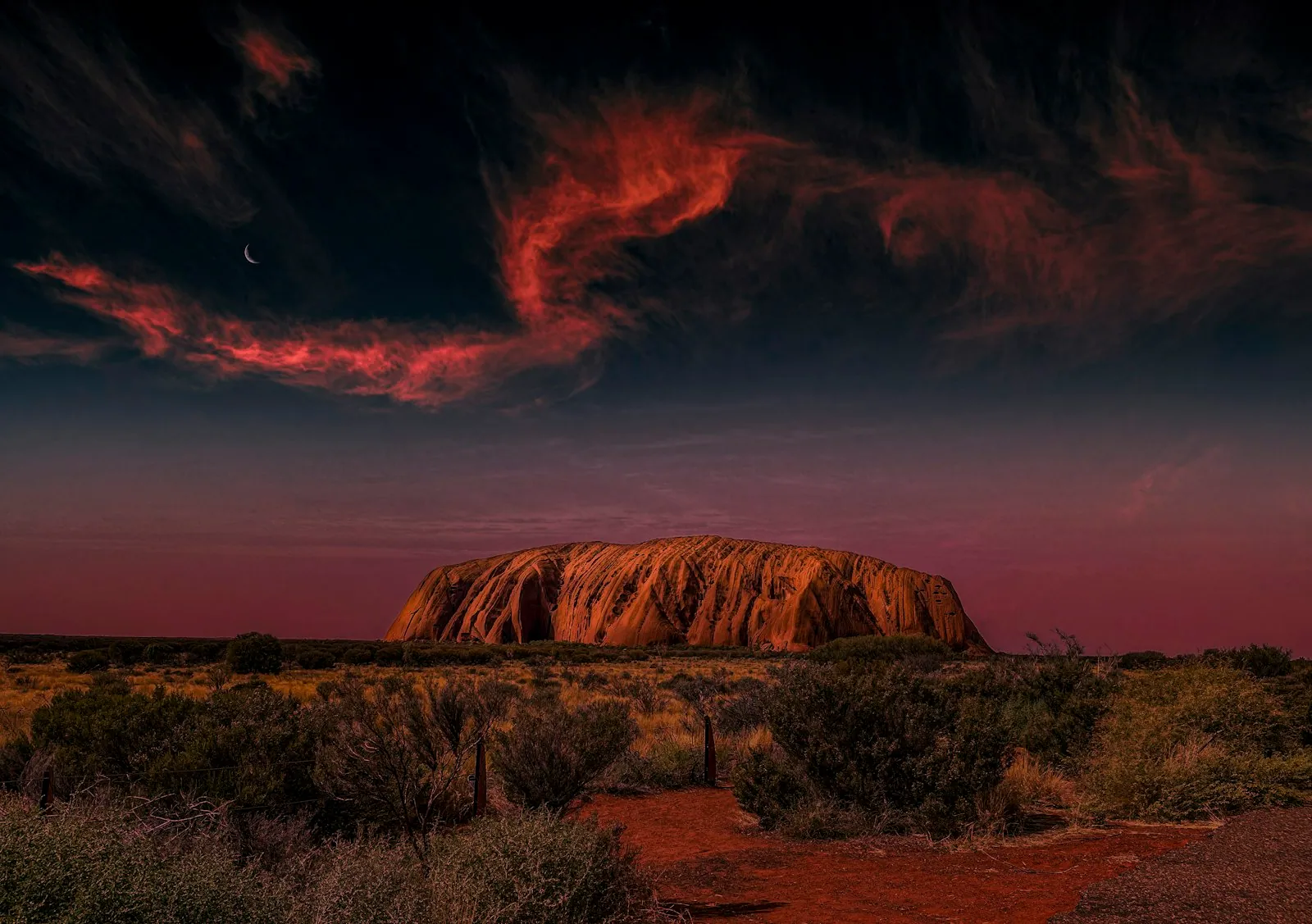 Uluru rising from the red desert under a clear blue sky in the Northern Territory